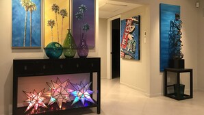 A hallway with a console table displaying colorful star-shaped lights, three framed paintings of palm trees, and a modern abstract sculpture.