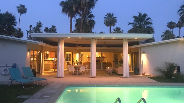 A modern house with a pool, covered patio, and palm trees.