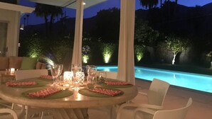 An outdoor dining area with a pool in the background.