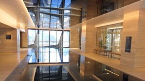 A modern interior with a reflective floor, glass walls, and a staircase leading to an upper level.