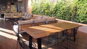 A modern outdoor seating area with a wooden table and chairs, a sofa with cushions, and a green vertical garden wall.