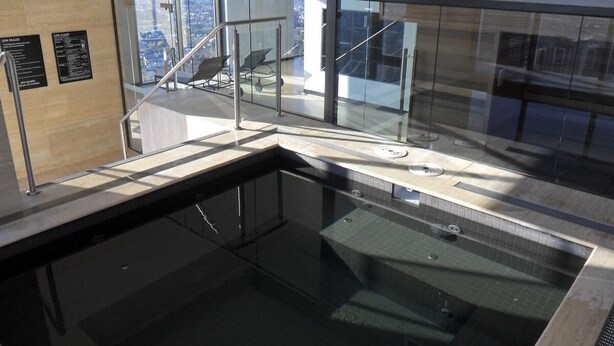 A modern indoor pool area with glass walls, a view of the city, and a staircase leading to an upper level.