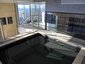 Un área de piscina interior moderna con paredes de vidrio, vistas a la ciudad y una escalera que lleva a un nivel superior.