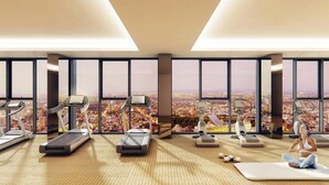 A high-rise gym with treadmills, a stationary bike, and a yoga mat area, overlooking a cityscape.