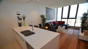 A modern kitchen with a central island, a dining area with a sofa, and large windows offering a city view.