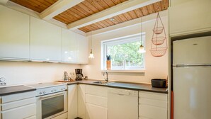 A modern kitchen with white cabinetry, a wooden ceiling, a window with a view of greenery, and a hanging light fixture.