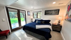 A bedroom with a large bed, a nightstand, a red bench, and a view of the outdoors through a sliding glass door. - Stillwater River Escape, Amazing Views, Secluded! (Whitefish)