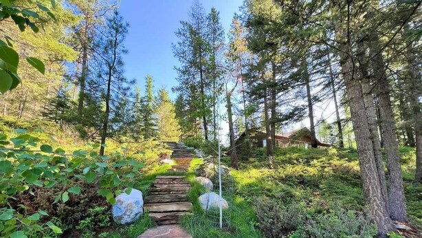 A stone pathway leading through a forested area with trees and greenery. - Stillwater River Escape, Amazing Views, Secluded! (Whitefish)