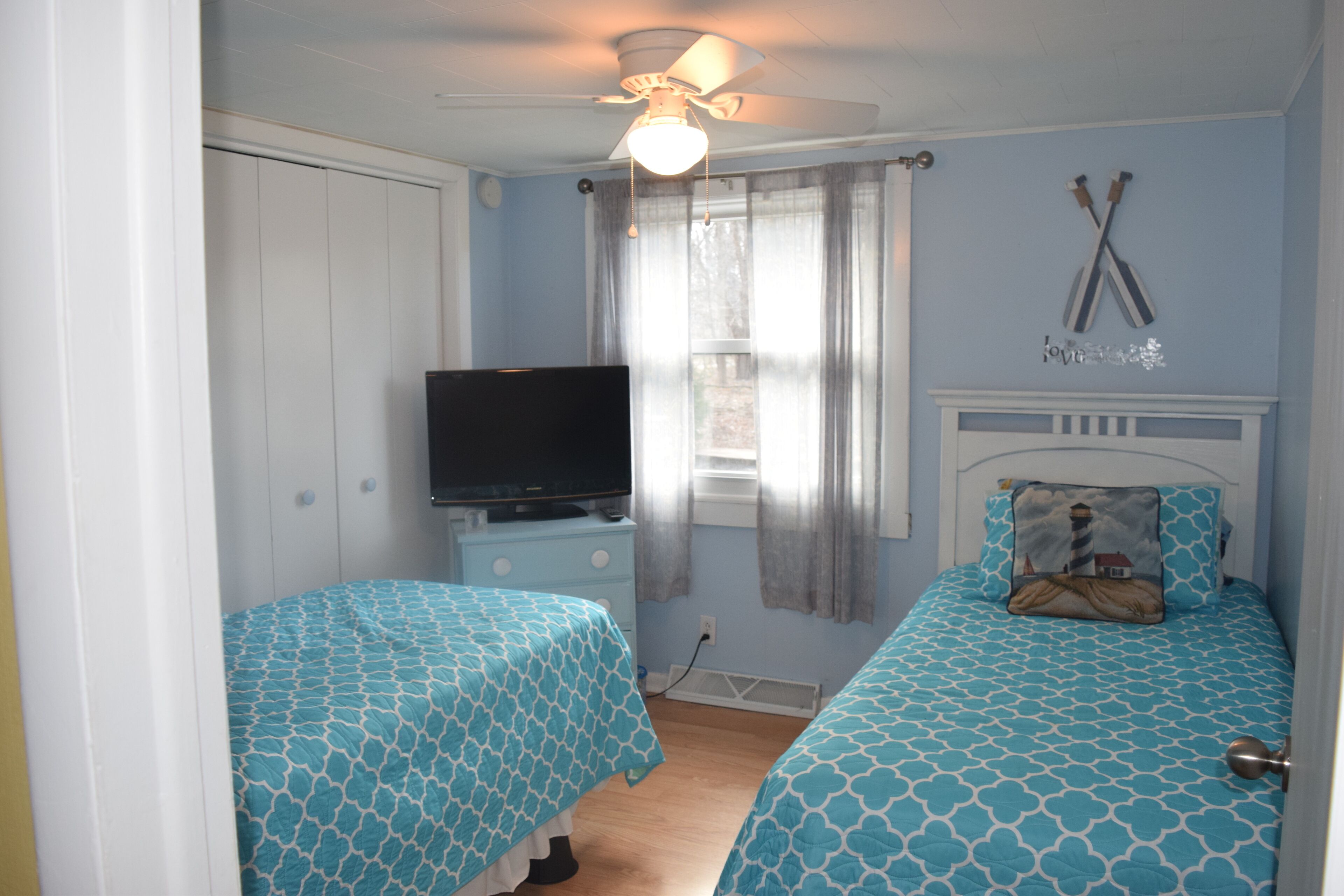 A bedroom with two beds, a TV, and a ceiling fan.