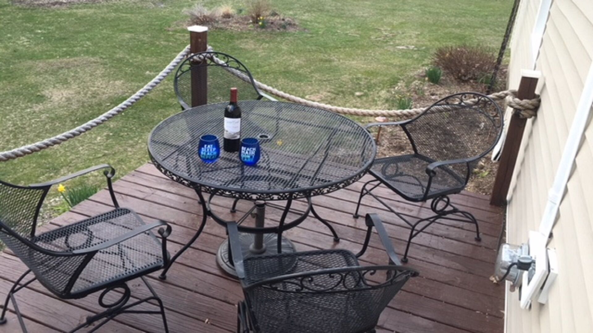 Une terrasse avec une table ronde et quatre chaises, entourée d’une barrière faite de cordes.
