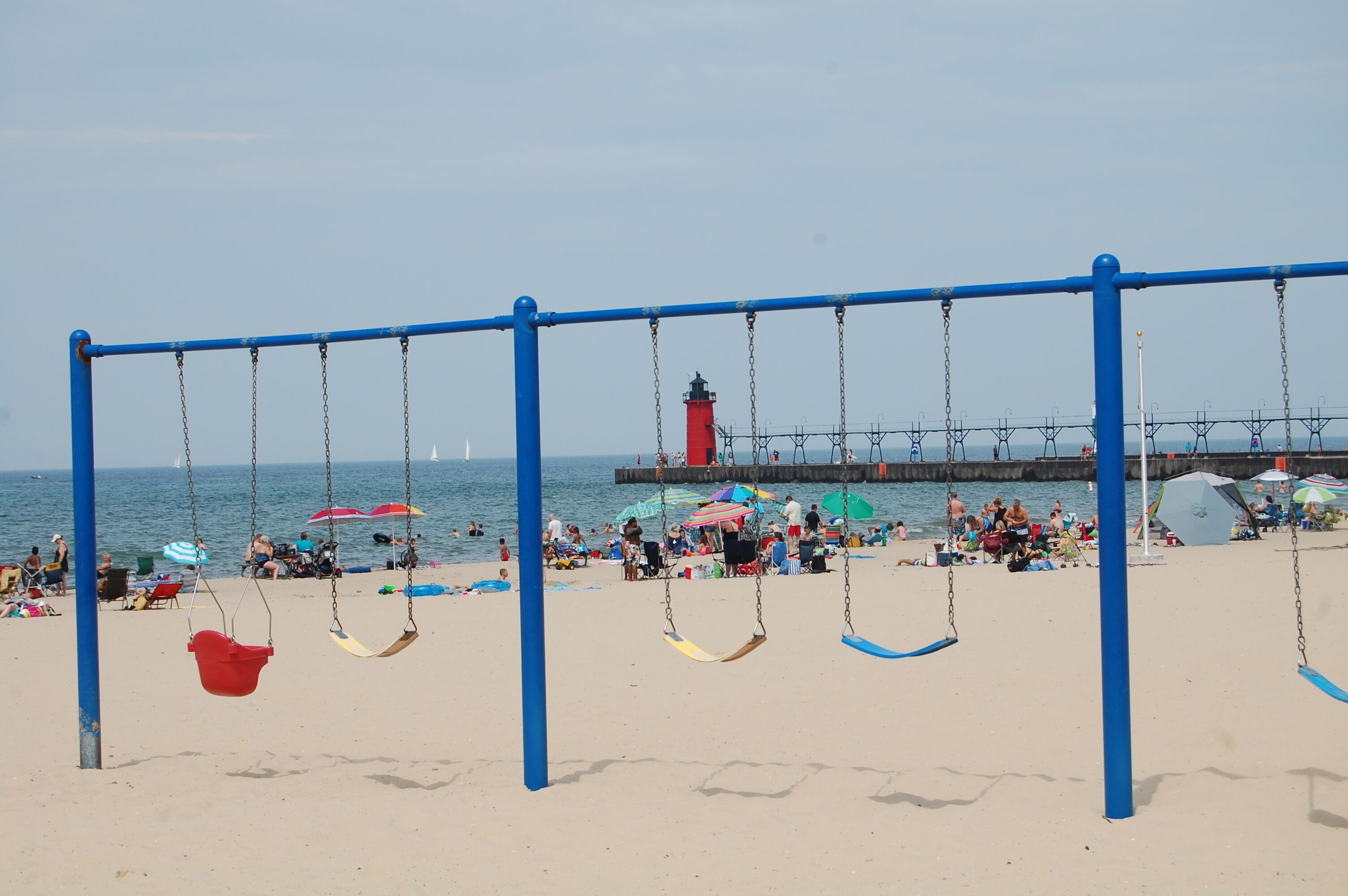 Une plage avec des balançoires, des parasols et une jetée en arrière-plan.