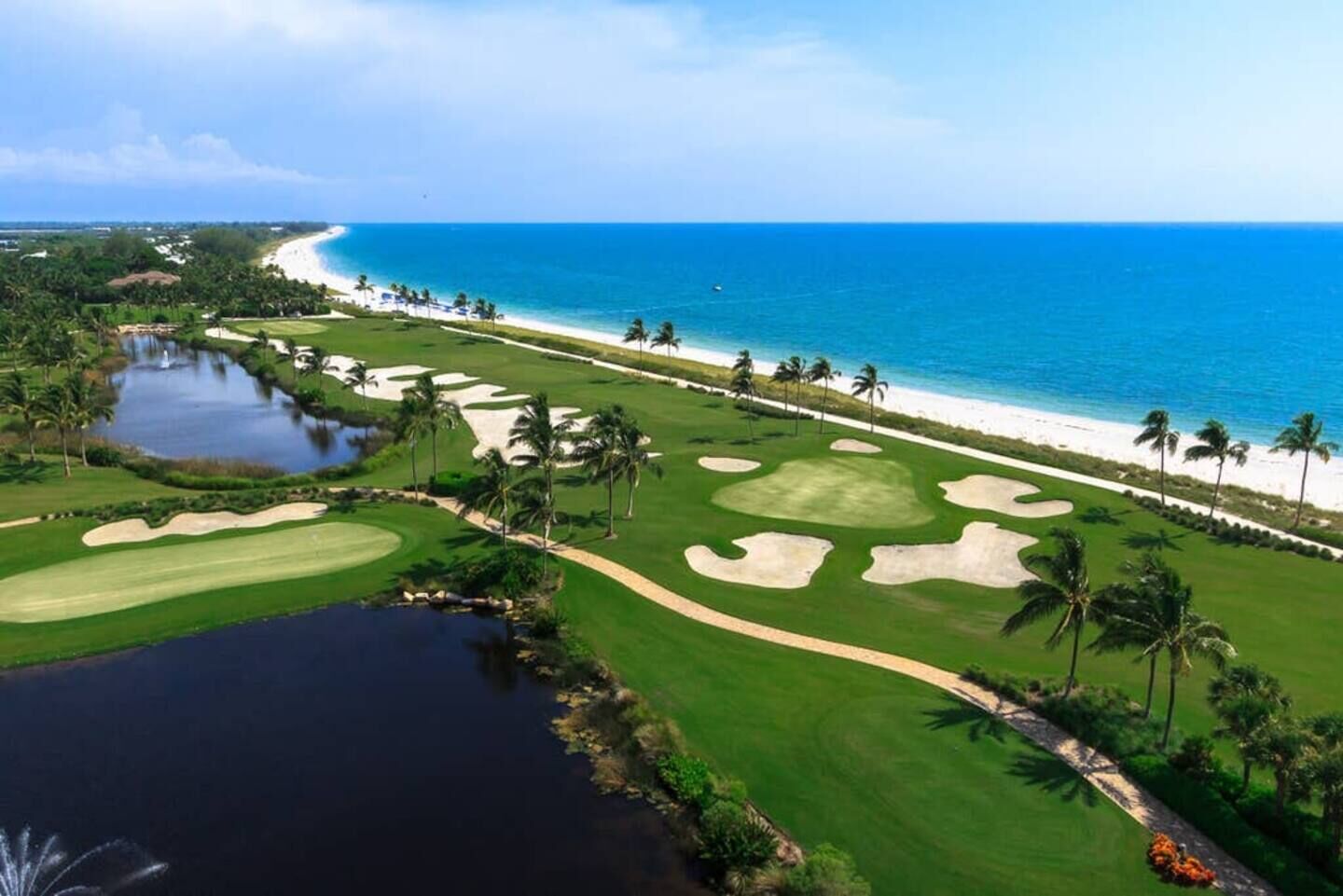 A golf course with a beach view, palm trees, and a water body.