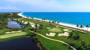 Un campo de golf con vista al mar, palmeras y una masa de agua.