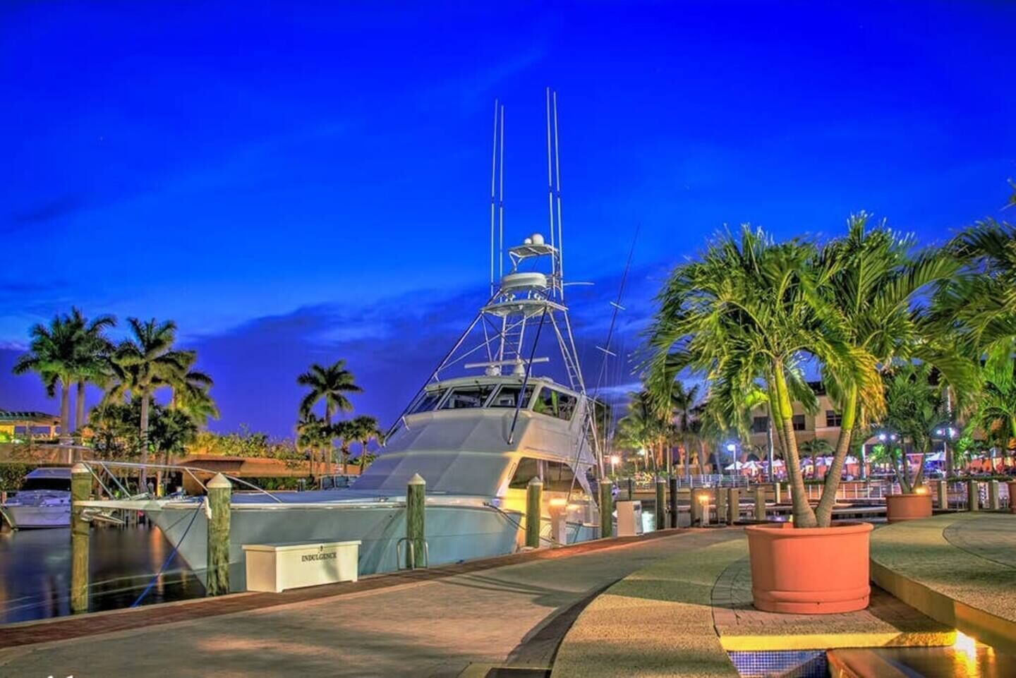 A large yacht docked at a marina with palm trees and a waterfront view.