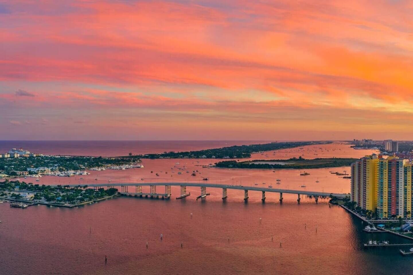 Vista aérea de una ciudad costera con un puente destacado, un puerto deportivo y edificios altos.