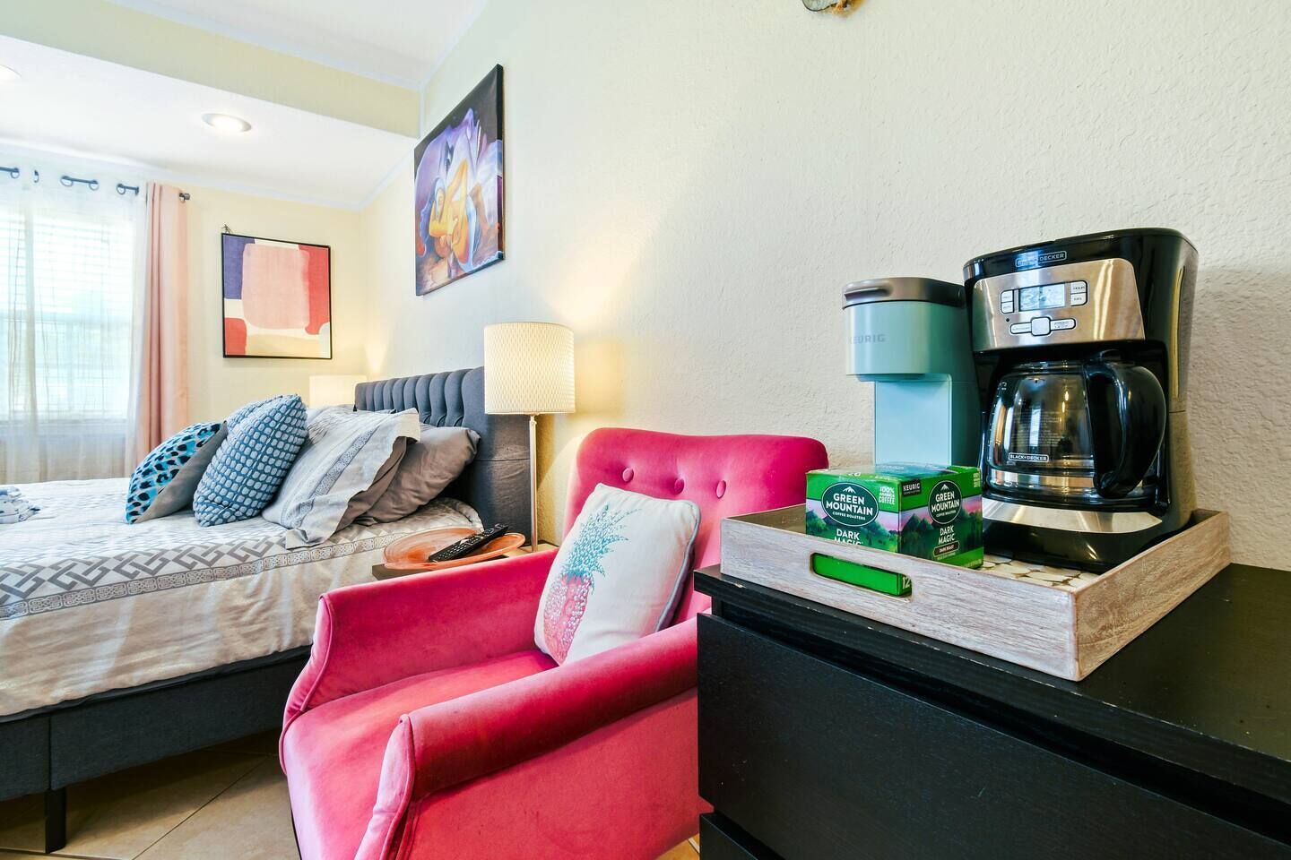 Ein Hotelzimmer mit einem Bett, einem roten Sessel, einer Kaffeemaschine und einer Packung Green Mountain Dark Magic Kaffee.