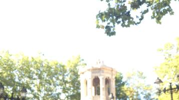Un grupo de personas bailando en una plaza pública con un monumento histórico al fondo.