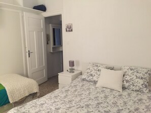 Une chambre à coucher comprenant un lit, une table de chevet avec une lampe, une armoire et une porte donnant sur une autre pièce.