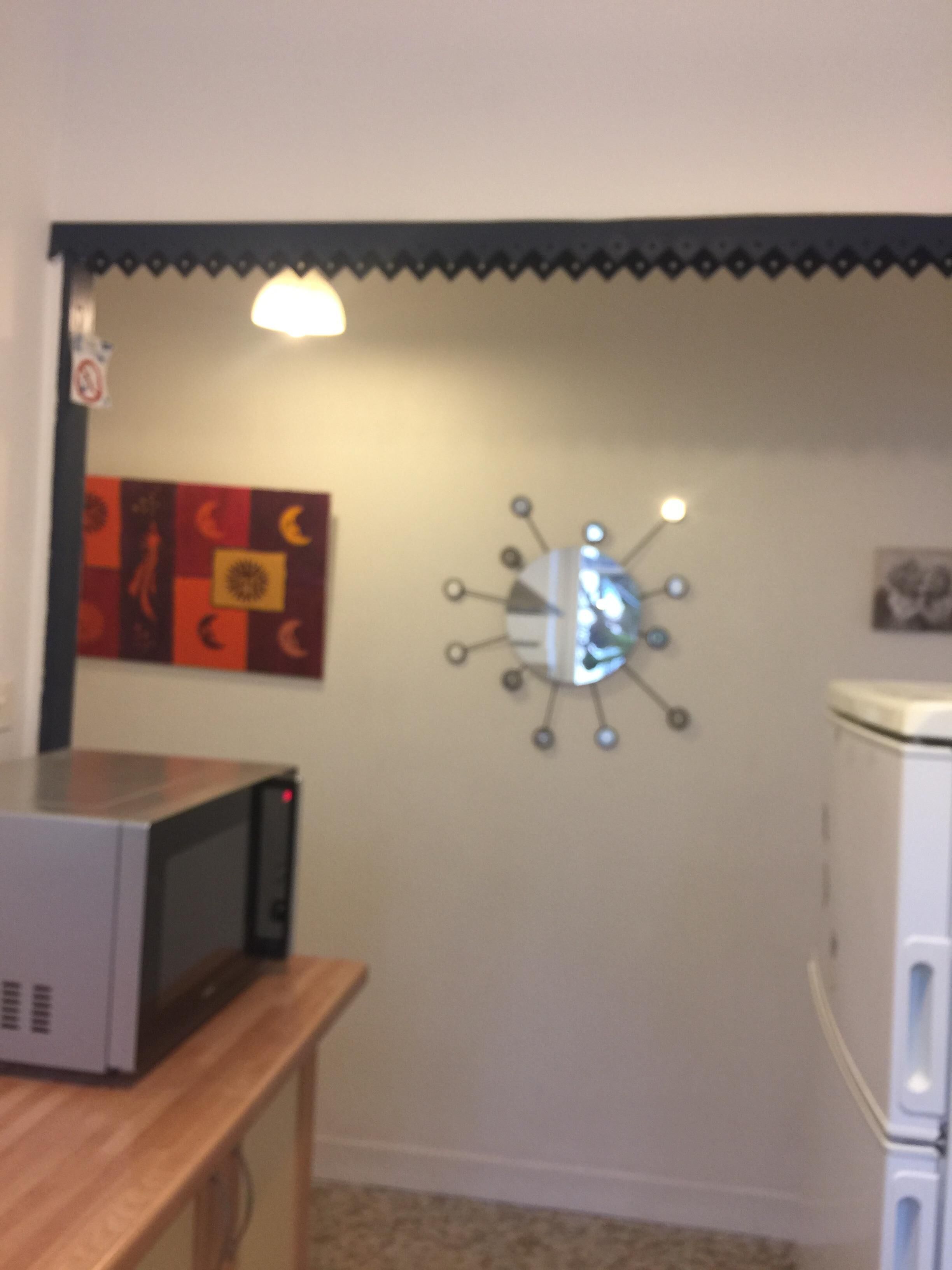A kitchen with a microwave on a wooden counter, a wall clock, and a refrigerator.
