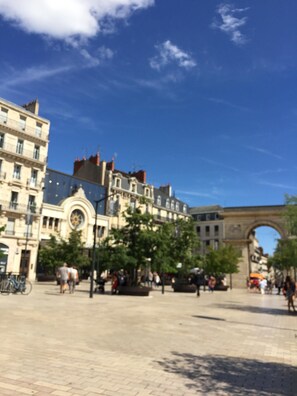 Une place publique dotée d’une architecture historique remarquable, notamment une imposante arche et des bâtiments de style classique.