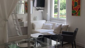 Une pièce moderne avec une table à manger en verre, un canapé, un téléviseur fixé au mur et une fenêtre donnant sur un paysage verdoyant.