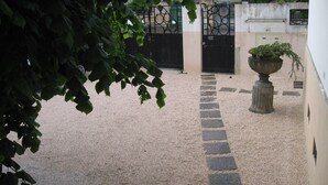 Une cour avec un chemin de gravier, un pot de fleurs et un portail noir.