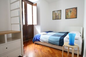 Ein Schlafzimmer mit einem Bett, Holzboden, einer weißen Kommode, einem kleinen Hocker und zwei Bildern an der Wand.