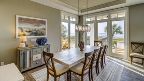A dining area with a large table, chairs, a chandelier, and a view of the ocean. - Perfect 10 Sea Hawk-Spectacular Oceanfront Dream House in Absolute Best Location (Hilton Head Island)