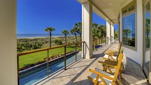 A balcony with a view of the beach, a pool, and wooden chairs. - Perfect 10 Sea Hawk-Spectacular Oceanfront Dream House in Absolute Best Location (Hilton Head Island)