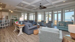 A spacious living room with a large gray sectional sofa, a smaller gray armchair, and a teal sofa facing a large window with a view of the beach. - Perfect 10 Sea Hawk-Spectacular Oceanfront Dream House in Absolute Best Location (Hilton Head Island)