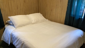 A neatly made bed with white linens in a room with wooden paneling on the walls.