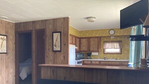 A compact kitchen with wooden cabinets, a built-in microwave, and a window with curtains.