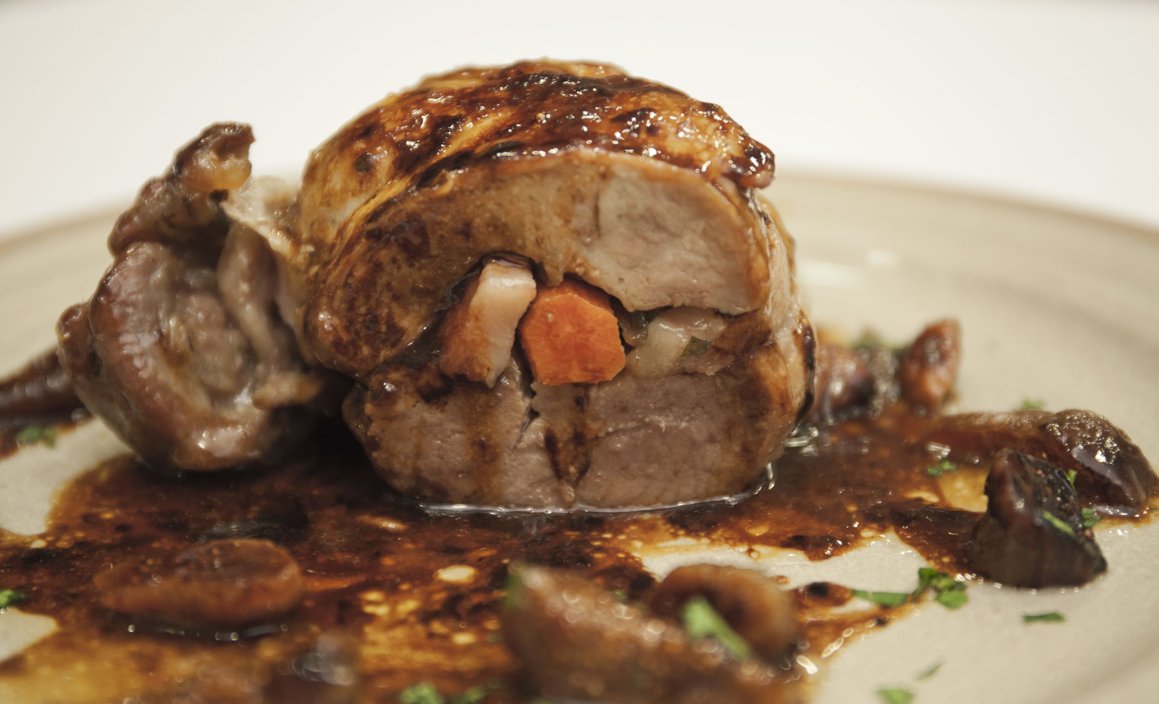 A dish with a meat centerpiece, surrounded by vegetables and sauce.
