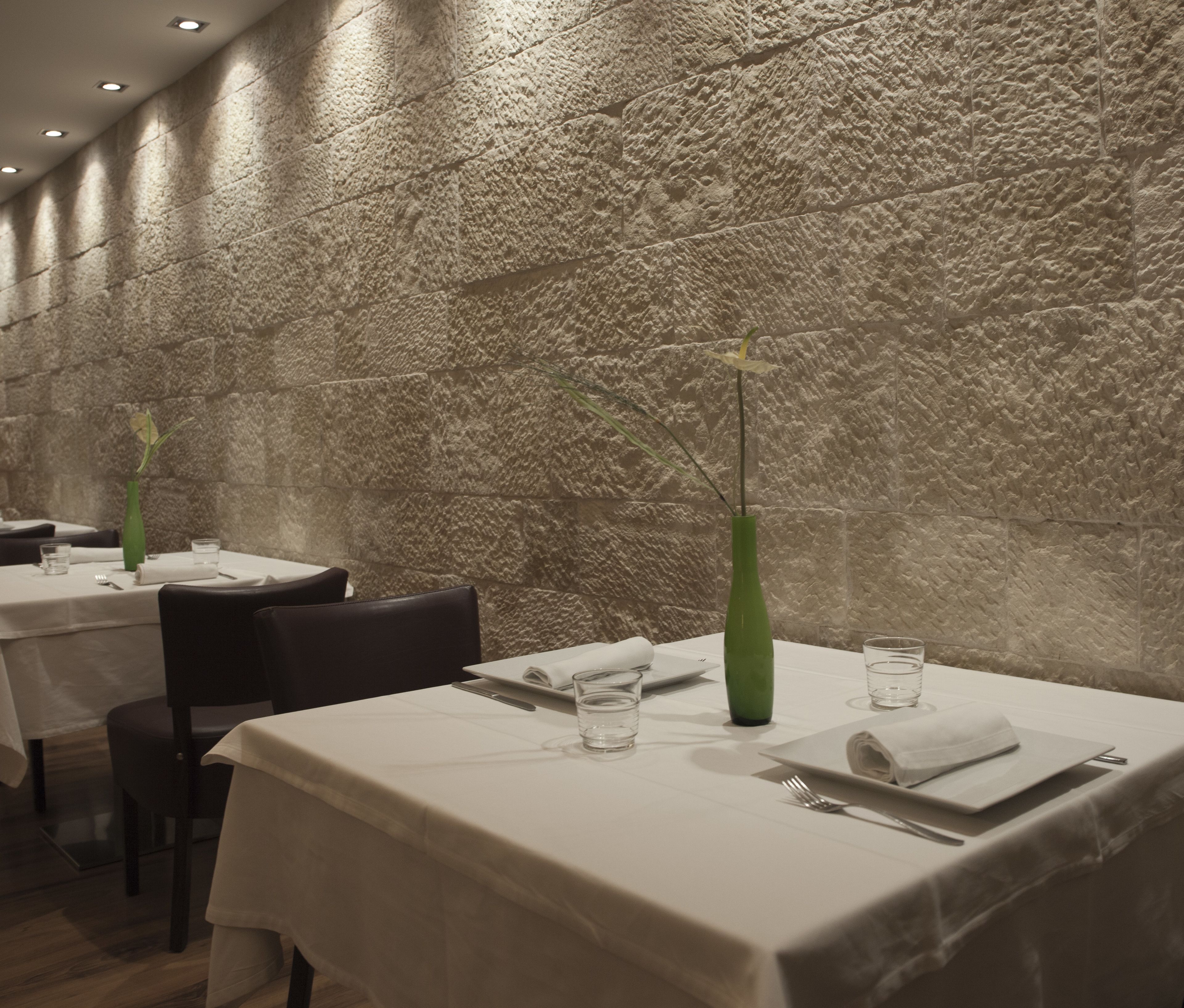 A restaurant interior with stone walls, white tablecloths, and green vases.