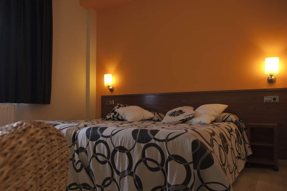 A neatly made bed with a patterned bedspread, two wall-mounted lamps, and a wooden headboard.