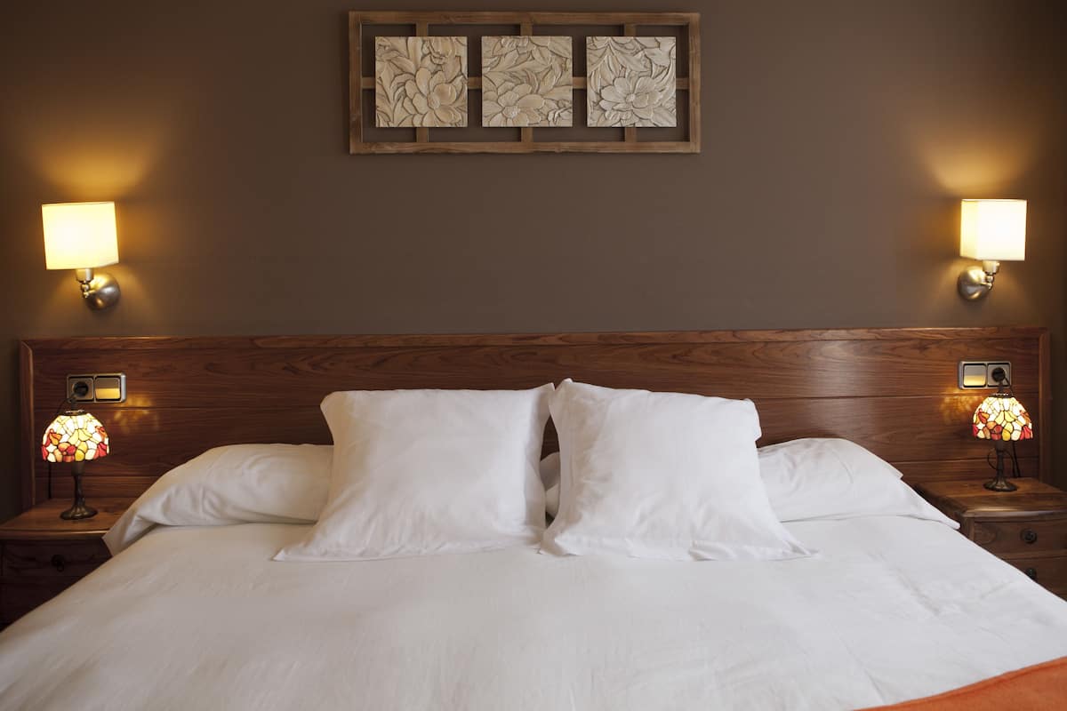 A neatly made bed with white linens, two wall-mounted lamps, and a wooden headboard.
