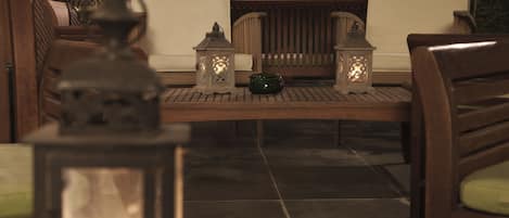 Un banc en bois, un bol vert, deux lanternes allumées et un sol carrelé.
