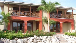 A two-story building with a balcony on the upper floor, a stone wall in front, and a pathway leading to the entrance.