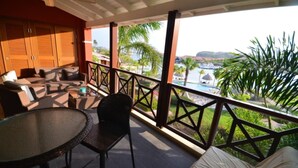 A balcony with a table and chairs, overlooking a pool and palm trees.
