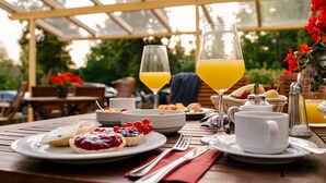 En morgenmadsopstilling med et bord dækket til to personer, herunder tallerkener med mad, et glas appelsinjuice, en kande og en kop.