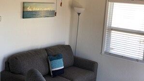 A living room with a gray sofa, a decorative pillow, a ceiling fan, and a window with blinds. - Private Beach Front Cottage- unit 1 (Fort Pierce)