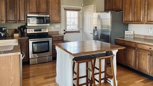 A kitchen with wooden cabinets, stainless steel appliances, a central island with stools, and a window with blinds. - Lakefront home near Mammoth Cave (Mammoth Cave)