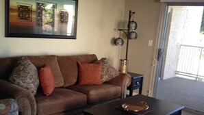 Ein Wohnzimmer mit einem braunen Sofa, gemusterten Kissen, einem schwarzen Couchtisch und einem gerahmten Bild an der Wand.
