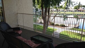 Ein Balkon mit Korbmöbeln, einem Glastisch und Blick auf einen Parkplatz sowie Gebäude.