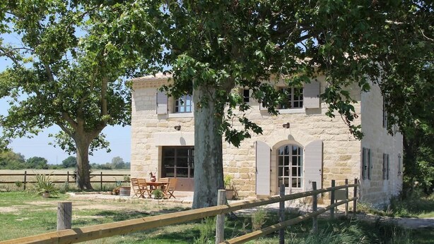 A stone building with a wooden fence, a dining table, and chairs outside.