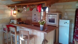 A rustic kitchen with a wooden bar, a white refrigerator, a microwave, and a stove. There are wooden chairs and a vase with flowers on the bar.