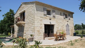 A stone building with a balcony, a door, and a table with chairs outside.