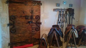 Una puerta de madera con ornamentación metálica detallada, un perchero con sillas de montar y un interruptor de luz fijado a la pared.