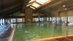 An indoor swimming pool with clear water, surrounded by lounge chairs and a stone pillar. - Oceanfront Condo with Fantastic Views (Kure Beach)