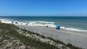 A beach with a sandy shore, a few umbrellas, and a clear blue sky. - Oceanfront Condo with Fantastic Views (Kure Beach)